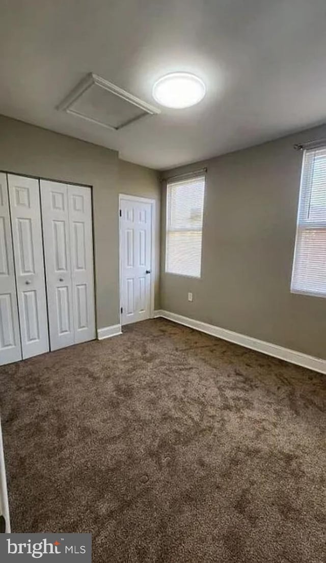 unfurnished bedroom with attic access, baseboards, multiple closets, and dark colored carpet