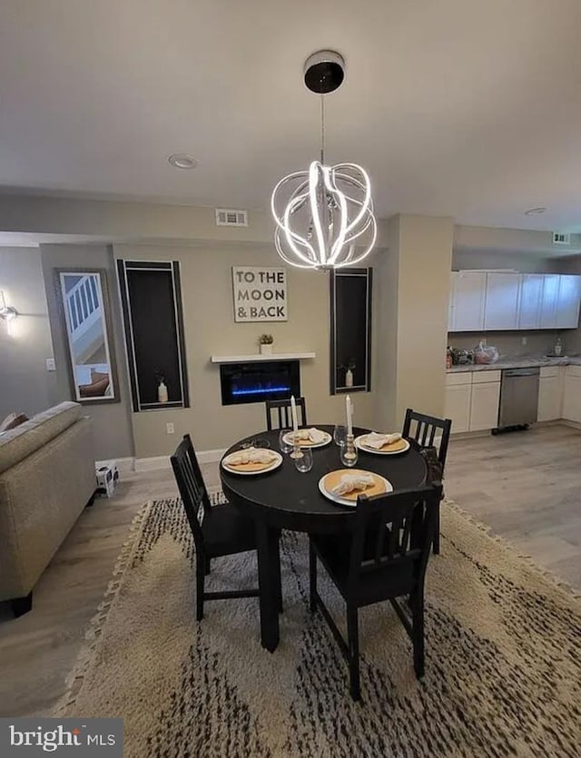 dining area with baseboards, light wood-type flooring, visible vents, and an inviting chandelier