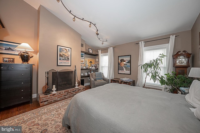 bedroom featuring multiple windows, a brick fireplace, dark wood-type flooring, and lofted ceiling