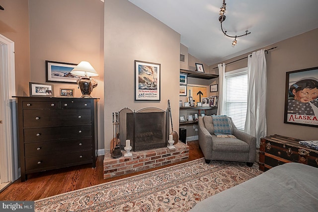 bedroom with lofted ceiling, a brick fireplace, and wood finished floors