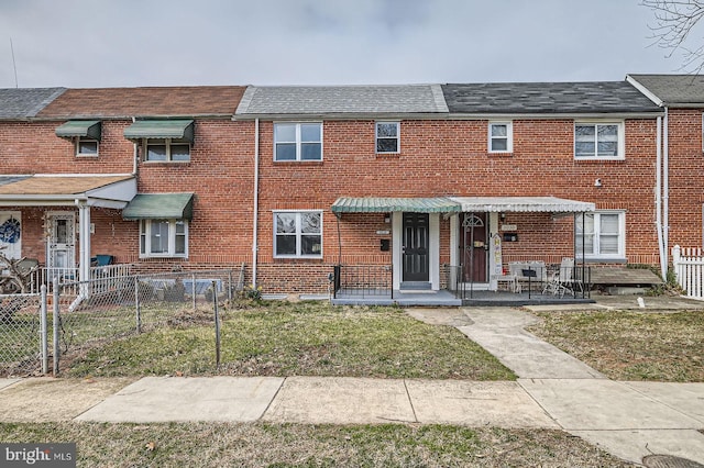 multi unit property with a gate, brick siding, a shingled roof, and fence