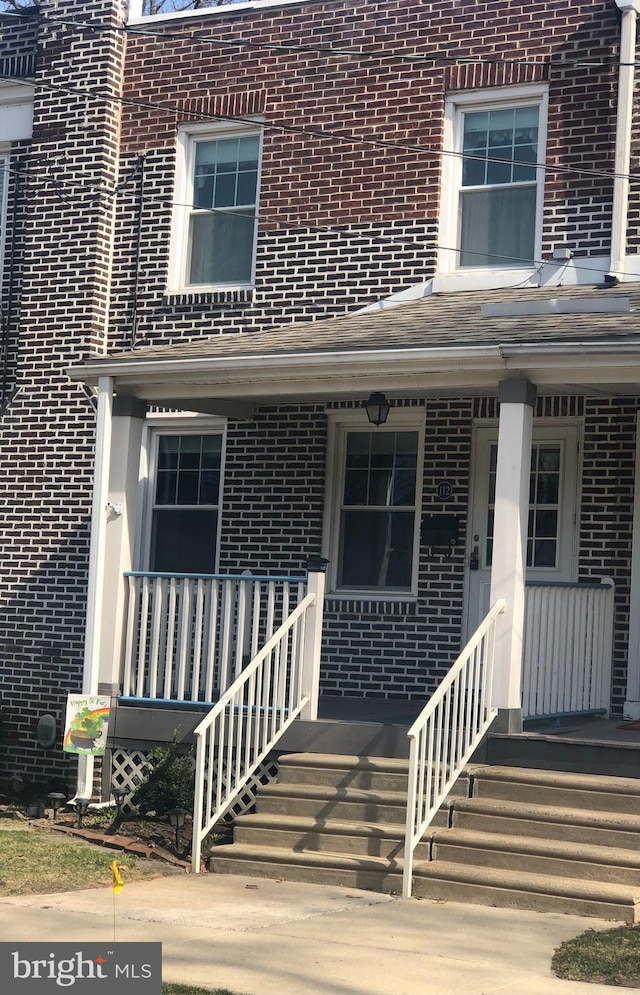 view of exterior entry with brick siding and a porch