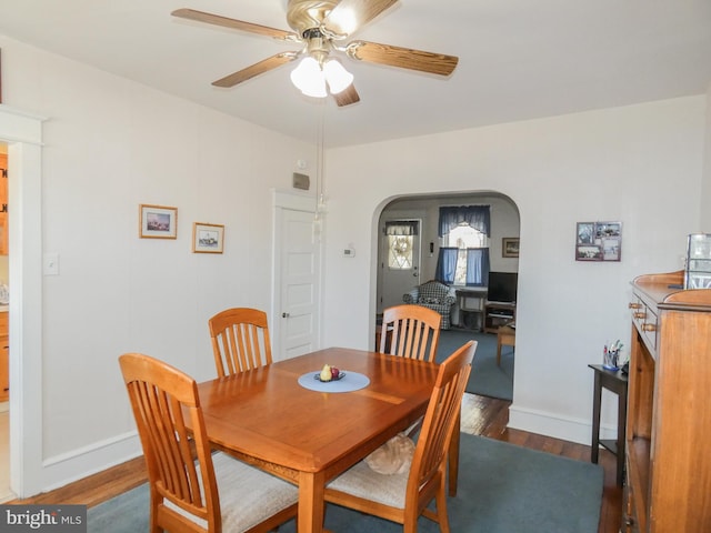 dining space featuring wood finished floors, a ceiling fan, arched walkways, and baseboards