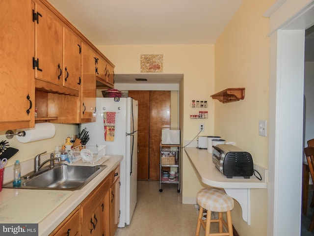 kitchen featuring light floors, light countertops, brown cabinets, freestanding refrigerator, and a sink