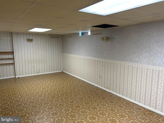 finished basement with wallpapered walls, visible vents, baseboards, and a drop ceiling