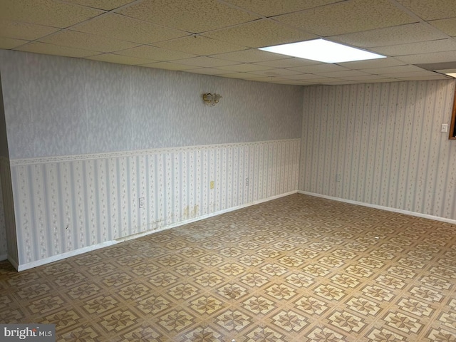 empty room featuring a drop ceiling, wallpapered walls, and baseboards