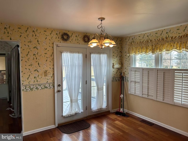 doorway to outside with visible vents, wood finished floors, an inviting chandelier, wallpapered walls, and baseboards