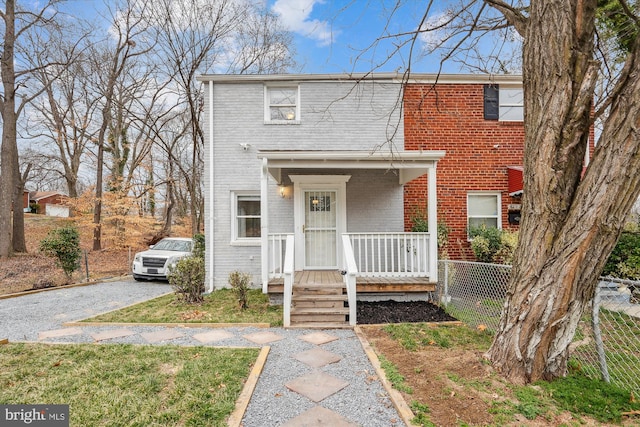 view of front facade with brick siding, a porch, gravel driveway, and fence