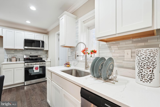 kitchen featuring dark wood-style flooring, a sink, ornamental molding, stainless steel appliances, and white cabinetry