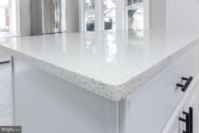 interior details featuring white cabinetry, light stone countertops, and freestanding refrigerator