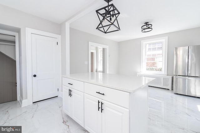 kitchen featuring radiator, freestanding refrigerator, white cabinetry, decorative light fixtures, and marble finish floor