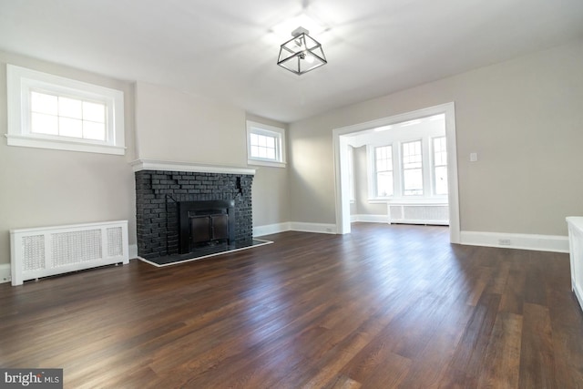 unfurnished living room with baseboards, radiator, a brick fireplace, and dark wood-style floors