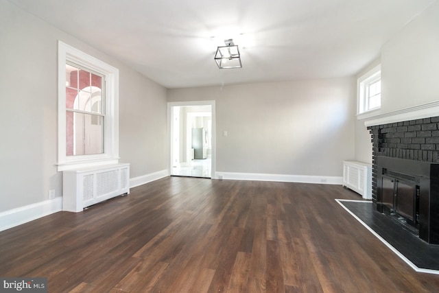 unfurnished living room with dark wood-type flooring, a brick fireplace, radiator, and baseboards