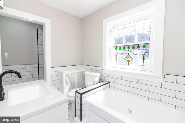 full bathroom featuring tile walls, a wainscoted wall, toilet, a garden tub, and vanity