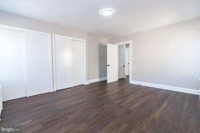 unfurnished bedroom with dark wood-type flooring, baseboards, and two closets