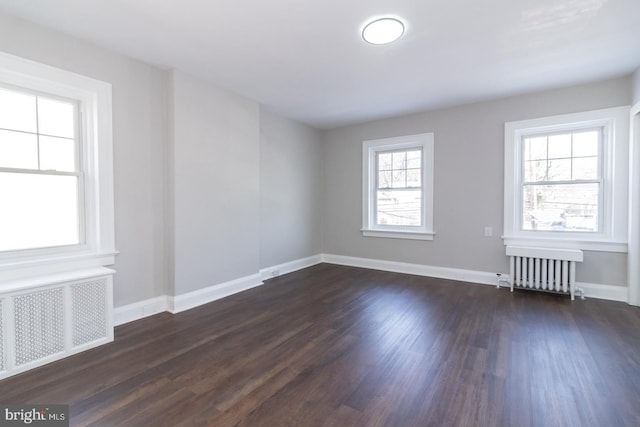 unfurnished room featuring baseboards, dark wood-type flooring, and radiator