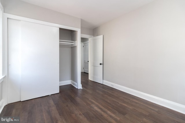 unfurnished bedroom featuring a closet, baseboards, and dark wood-style flooring