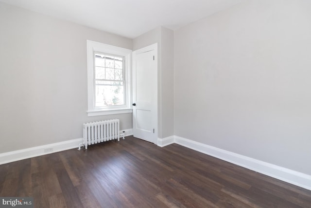 empty room featuring baseboards, dark wood-style flooring, and radiator heating unit