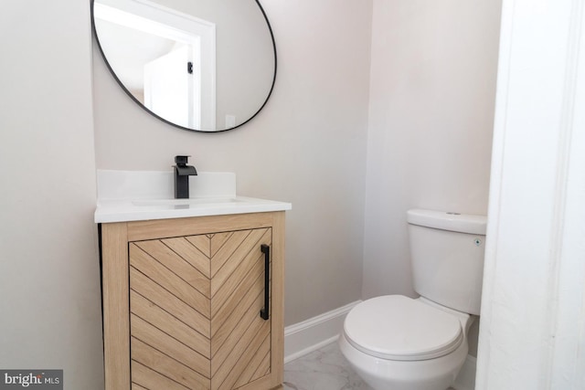 half bath featuring baseboards, marble finish floor, vanity, and toilet