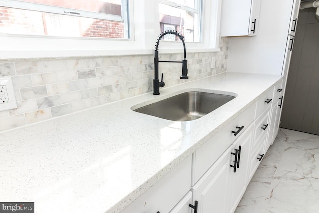 kitchen featuring marble finish floor, light stone countertops, white cabinetry, and a sink