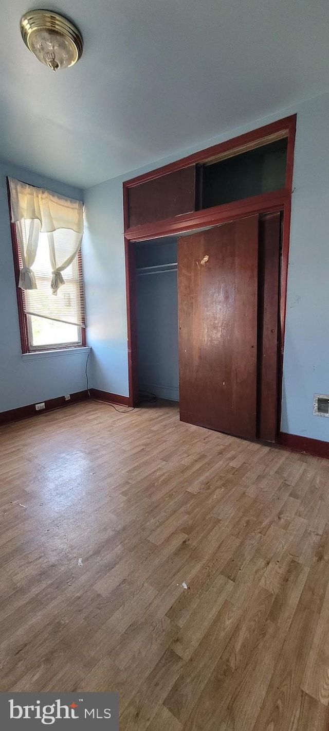 unfurnished bedroom with baseboards, a closet, wood finished floors, and visible vents