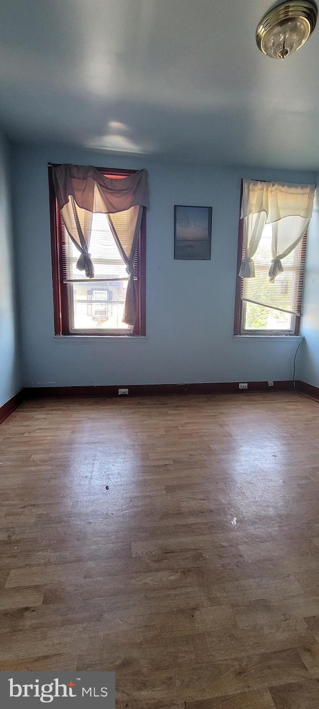 empty room with a healthy amount of sunlight, baseboards, and wood finished floors
