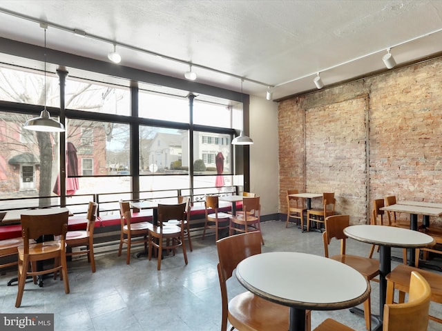 dining room featuring rail lighting, brick wall, and a textured ceiling