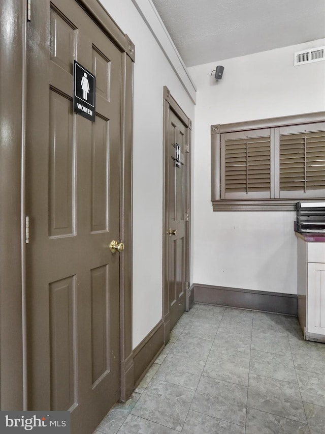 hallway with light tile patterned floors, visible vents, and baseboards