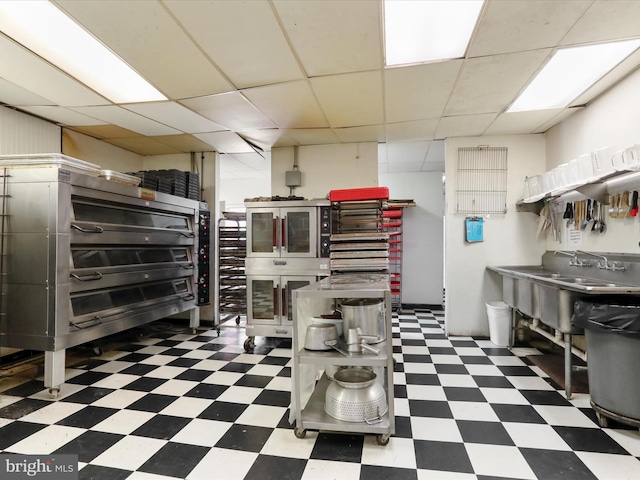 interior space featuring tile patterned floors, glass insert cabinets, and a paneled ceiling