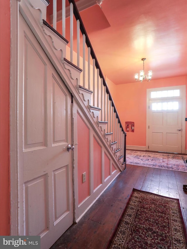 foyer entrance featuring stairs, baseboards, dark wood-style flooring, and a chandelier