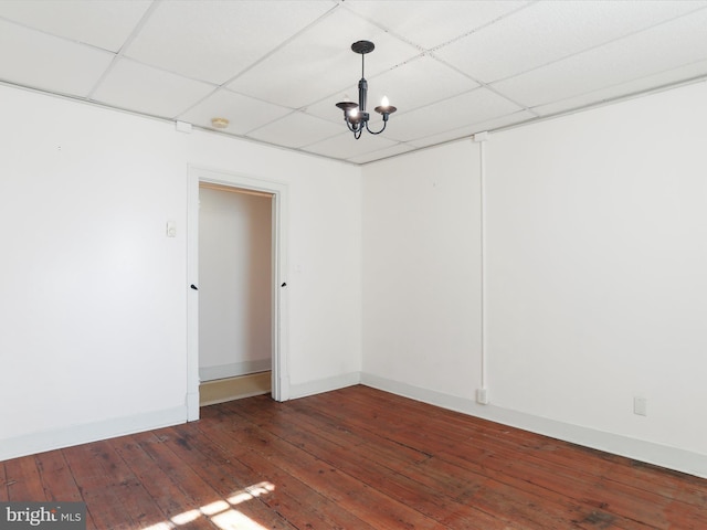 unfurnished room featuring a notable chandelier, a drop ceiling, baseboards, and dark wood-style flooring