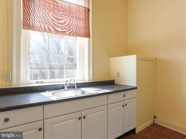 kitchen with a sink, dark countertops, white cabinets, and dark tile patterned flooring