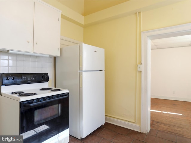 kitchen with backsplash, range with electric cooktop, dark tile patterned floors, freestanding refrigerator, and white cabinetry