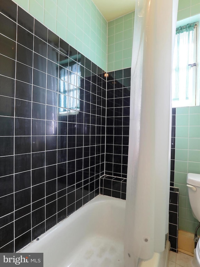 bathroom featuring tile patterned floors, shower / bath combo with shower curtain, toilet, and tile walls