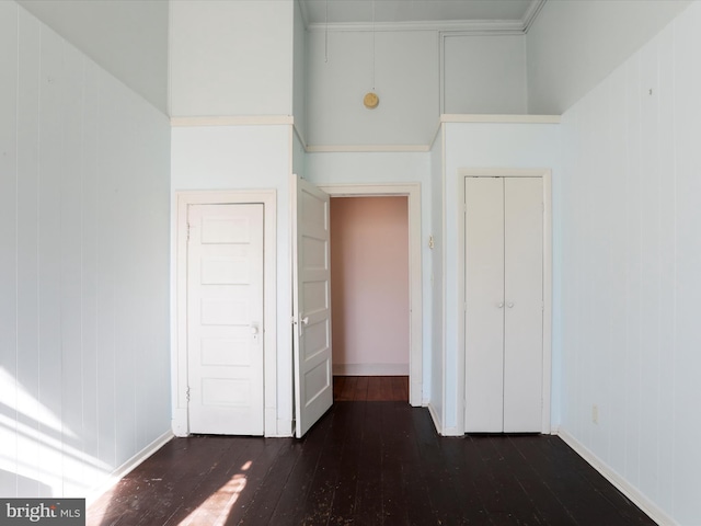 unfurnished bedroom featuring hardwood / wood-style floors, baseboards, a closet, and a towering ceiling