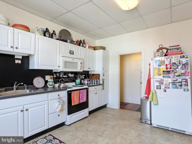 kitchen with white appliances, a sink, a paneled ceiling, white cabinetry, and dark countertops