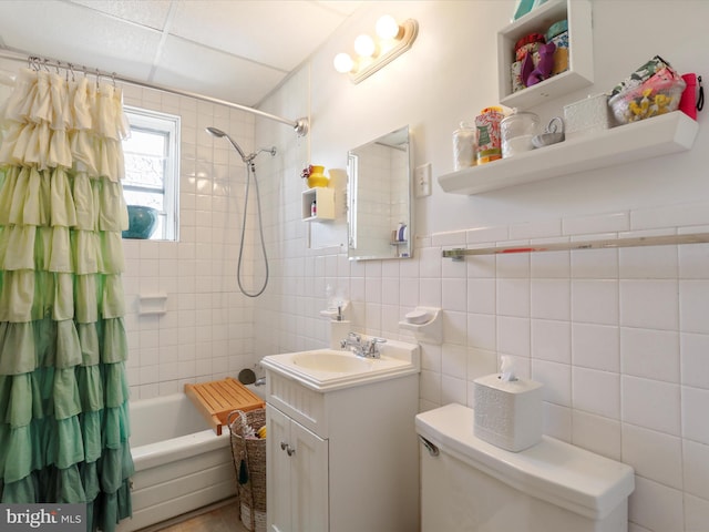 bathroom featuring tile walls, a wainscoted wall, toilet, shower / tub combo with curtain, and vanity