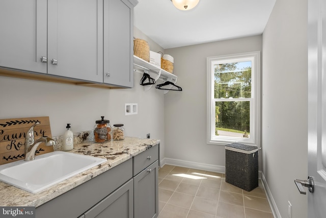 laundry area featuring light tile patterned floors, baseboards, cabinet space, a sink, and washer hookup