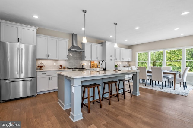 kitchen featuring dark wood finished floors, high end refrigerator, decorative backsplash, wall chimney exhaust hood, and a sink