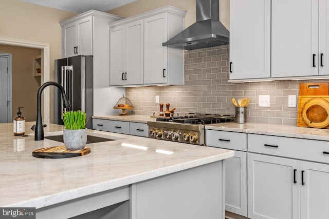 kitchen with wall chimney range hood, light stone countertops, high end fridge, and backsplash