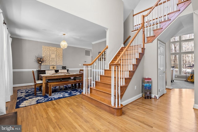 staircase with an inviting chandelier, wood finished floors, visible vents, and ornamental molding