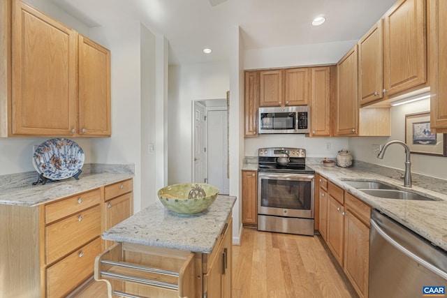 kitchen with a sink, light stone countertops, appliances with stainless steel finishes, and light wood-style flooring