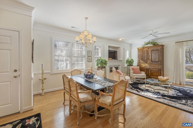 dining area featuring light wood-type flooring, visible vents, ornamental molding, and ceiling fan with notable chandelier