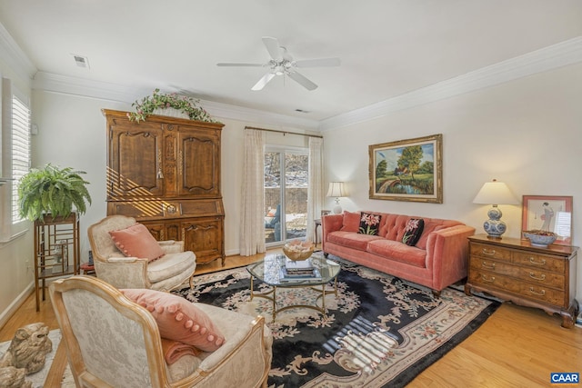 living room featuring light wood-style flooring, ornamental molding, a ceiling fan, and a healthy amount of sunlight