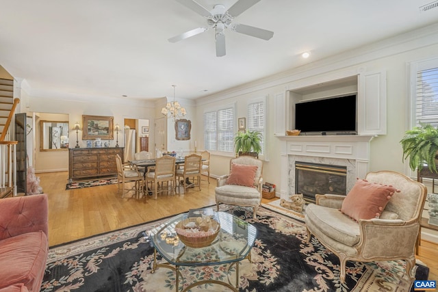 living room featuring ornamental molding, wood finished floors, a fireplace, and ceiling fan with notable chandelier