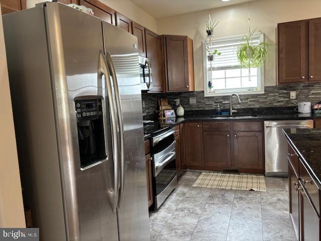 kitchen with a sink, stainless steel appliances, decorative backsplash, and dark stone counters