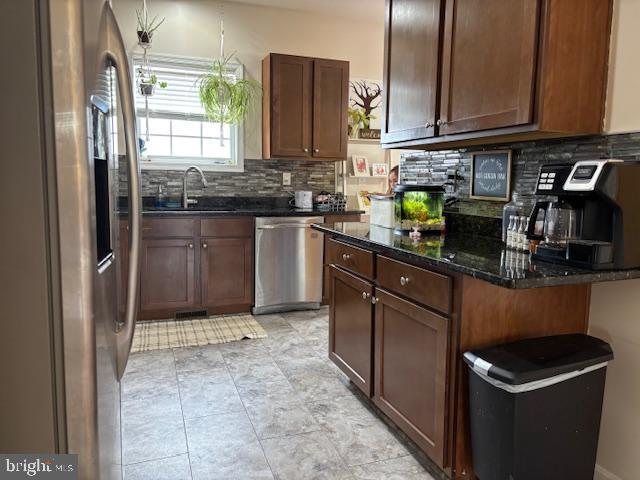 kitchen with a sink, dark stone countertops, tasteful backsplash, and stainless steel appliances