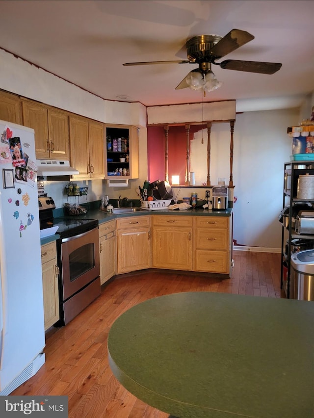 kitchen featuring stainless steel electric stove, freestanding refrigerator, a sink, under cabinet range hood, and dark countertops