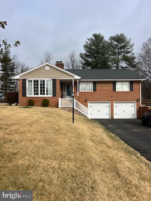 ranch-style house with an attached garage, driveway, a front yard, brick siding, and a chimney