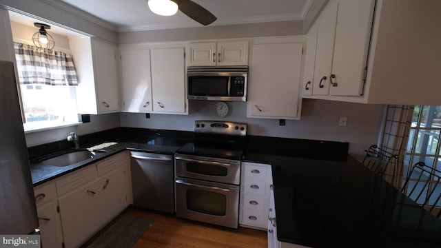 kitchen featuring white cabinets, ornamental molding, dark countertops, appliances with stainless steel finishes, and a sink